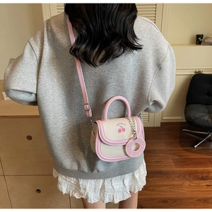 Detail of cream saddle bag with pink strap featuring cherry print and donut charm