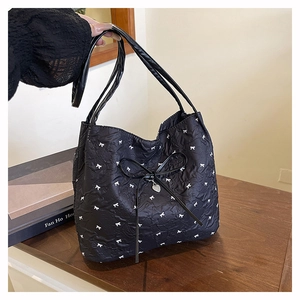 Detail der schwarzen Stepptasche mit weißen Schleifenmustern und silbernem Herzanhänger