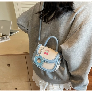 Detail showing blue and cream leather saddle bag with cherry print and donut pendant