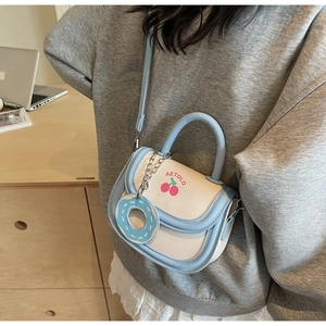 Detail of light blue and white saddle bag with cherry print and donut pendant charm