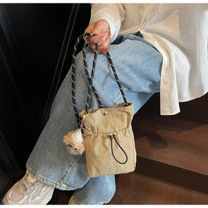 Detail der khakifarbenen Nylon-Beuteltasche mit gewebtem Gurt und Plüsch-Anhänger