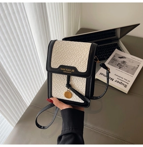 Detail of checkered leather phone bag with gold metal charm on a minimalist desk