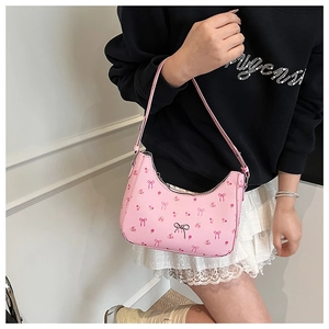 Detail of pink shoulder bag with floral print and silver bow charm on a model
