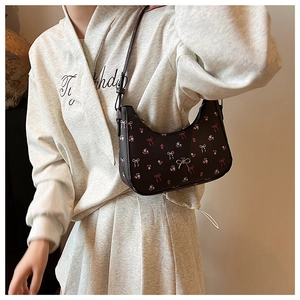 Detail of black underarm bag with floral print and 3D metal bow on the strap