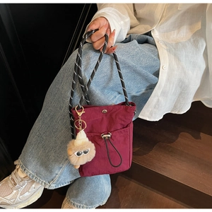 Detail der burgunderroten Nylon-Mini-Umhängetasche mit gewebtem Seilriemen und Plüschanhänger