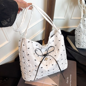 Weiße Stepptasche mit schwarzen Schleifenprints und großem Schleifenanhänger im Alltag