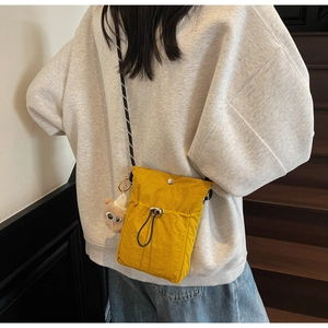 Detailaufnahme der neongelben Nylon-Umhängetasche mit Kordelzugtasche und Plüschanhänger