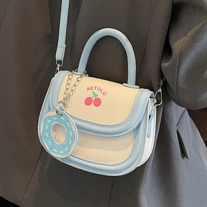 Cute cream saddle bag with cherry print and donut pendant, worn on a grey suit jacket