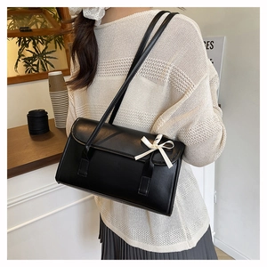 Elegant black shoulder bag with cream bow detail worn by a model in a minimalist setting
