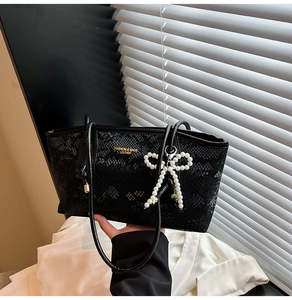 Detail of black lace texture tote bag featuring a large white pearl bow charm