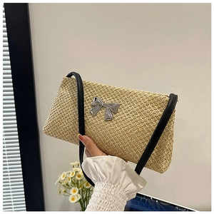 Detail of woven straw shoulder bag featuring a metallic silver bow and slim leather strap