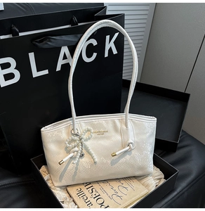Detail of cream faux-snake leather tote with pearl bow charm and knotted shoulder strap