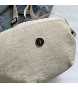 Détail du sac bandoulière en nylon beige avec texture plissée et logo en métal noir