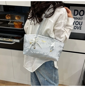 Detail of silver snake skin tote bag featuring pearl bow charm and knot shoulder strap