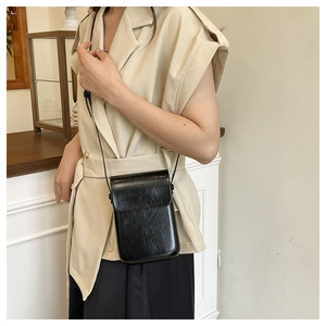 Detail of a black crossbody bag with pleated glossy finish worn on a waist level strap