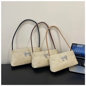 Straw shoulder bags with metallic bow detail and colorful straps shown on a desk
