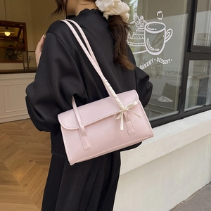 Elegant pink shoulder bag with bow detail and ribbon strap shown on a model