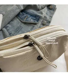 Détail des tirettes de fermeture en métal et texture nylon sur le sac bandoulière beige
