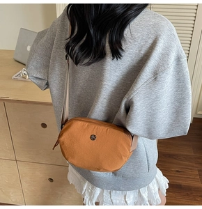 Détail du sac bandoulière en nylon caramel avec logo métallique rond en décor lifestyle