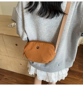 Détail du sac bandoulière en nylon caramel avec logo en métal rond et sangle tissée