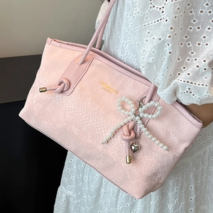 Pink snake-patterned tote bag with pearl bow charm and heart pendant worn on shoulder