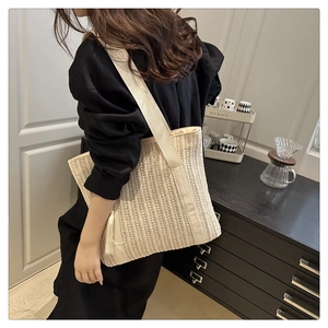 Close-up of beige woven tote bag featuring wide fabric straps and fringe tassel detail