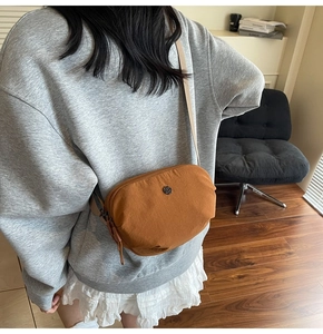 Vue latérale d'un sac bandoulière en nylon caramel porté par un mannequin en intérieur