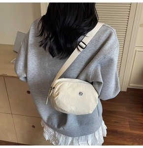 Sac bandoulière en nylon blanc cassé porté par un mannequin, design incurvé et sangle réglable