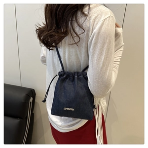 Dettaglio borsa a secchiello in denim blu con logo in metallo dorato e coulisse
