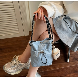 Nahaufnahme der hellblauen Nylon-Kordelzugtasche mit Plüschmonster-Anhänger und Webgriff