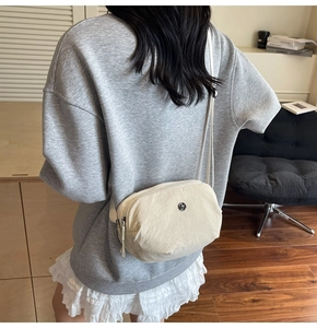 Mannequin portant un sac bandoulière en nylon blanc cassé dans un décor minimaliste