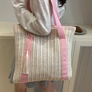 Woven straw tote bag with pink canvas straps and fringe tassel detail on a model