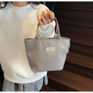 Close-up of a silver nylon tote bag with a FASHION label and durable fabric handles