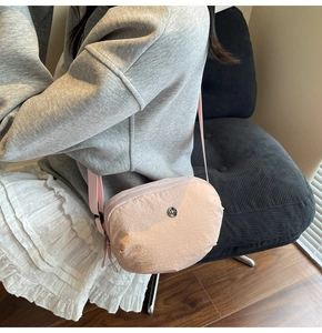 Détail du sac bandoulière en nylon rose clair montrant la texture plissée et le logo