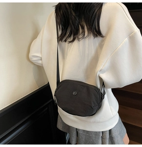 Vue arrière d'un sac bandoulière en nylon noir avec logo métallique rond et fermeture éclair