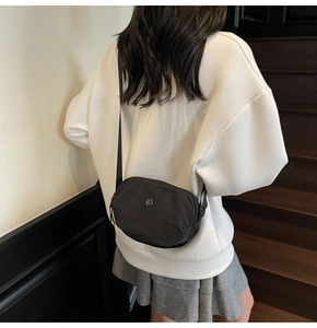 Détail d'un sac bandoulière en nylon noir avec logo en métal porté sur un sweat blanc