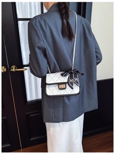 Close-up of white quilted chain bag with a decorative silk scarf and gold clasp detail