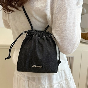 Schicke schwarze Denim-Beuteltasche mit Kordelzug und Metalllogo, von einem Model getragen