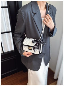 Detail of white quilted handbag with black trim, gold twist lock, and ribbon bow