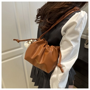 Detailed texture of brown pleated cloud shoulder bag with golden logo and plush charm