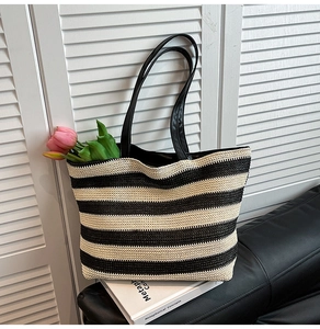 Detail of a black and white striped straw tote bag featuring thick woven texture and strap