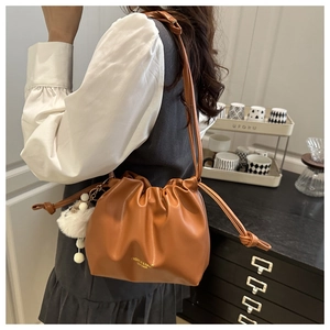 Detail of caramel leather drawstring bucket bag with a white pompom charm on a model