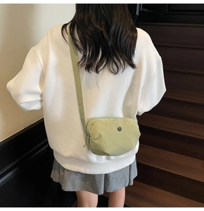 Détail du sac bandoulière en nylon vert clair avec double fermeture éclair sur vêtement clair