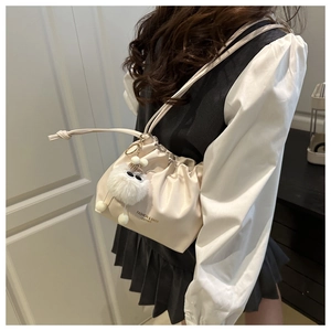 Detail view of cream drawstring bucket bag with pleated texture and plush charm accessory