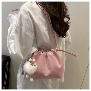 Pink drawstring bucket bag featuring golden logo lettering and white plush ball charm
