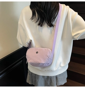 Gros plan d'un sac bandoulière violet en nylon avec logo métallique sur un mannequin