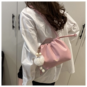Close-up of a pink pleated cloud bag with a white plush ball charm on a female model