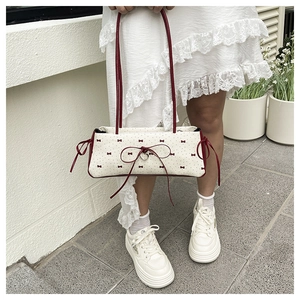 Détail du sac crème avec imprimé nœuds rouges et pendentif en métal en forme de cœur