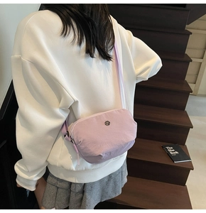 Détail d'un sac bandoulière en nylon violet clair avec logo en métal sur un escalier
