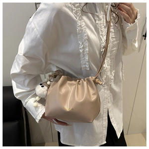 Detail of beige pleated bucket bag with gold lettering and white plush ball charm